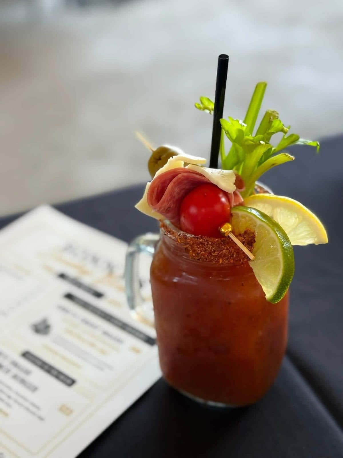 Sonny's Signature Bloody Mary in a spice-rimmed mason jar with prosciutto, aged cheese, olive, cherry tomato, celery and citrus