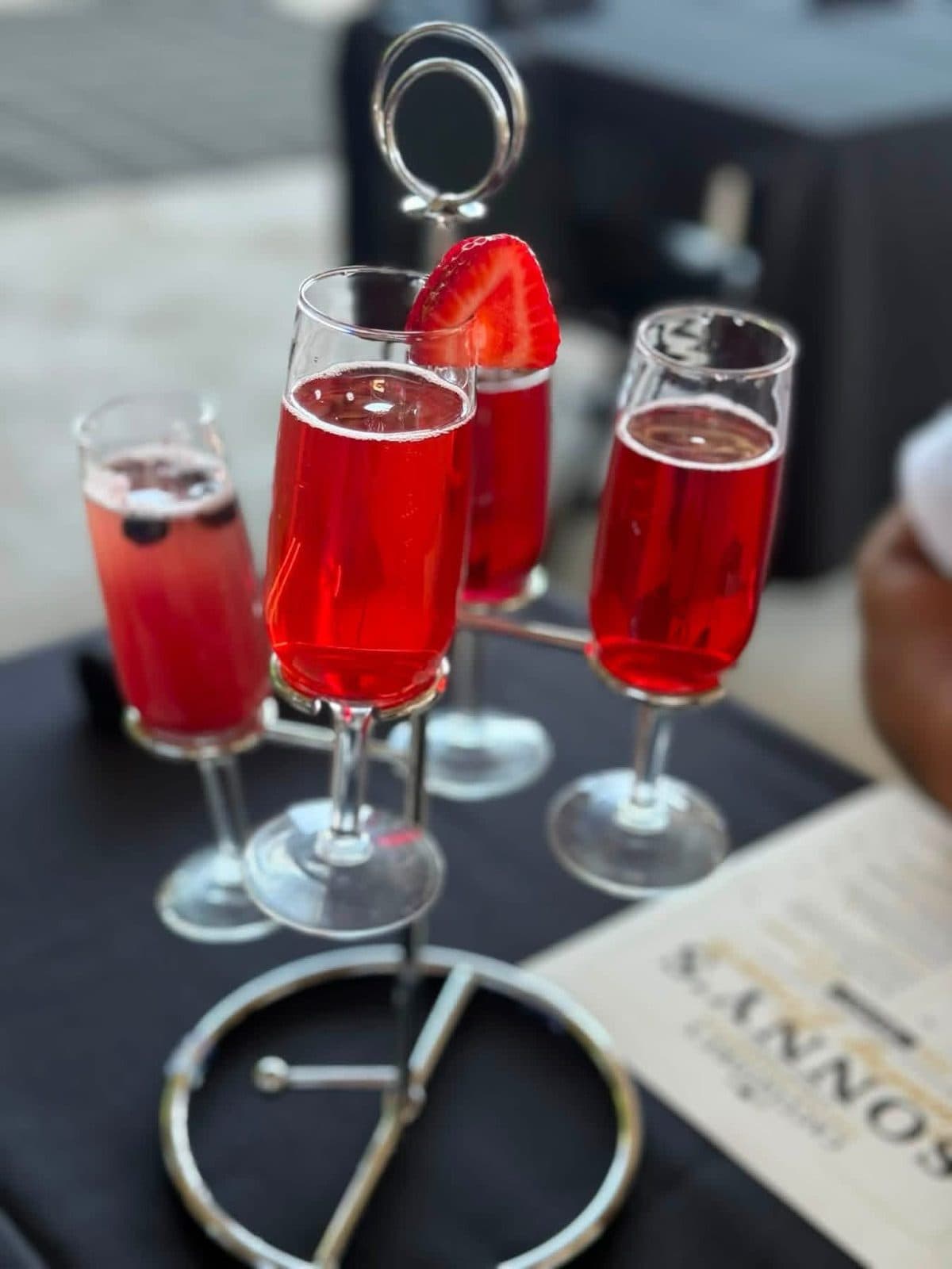 Mimosa flight served on a metal stand with four seasonal fruit flavors garnished with fresh strawberry
